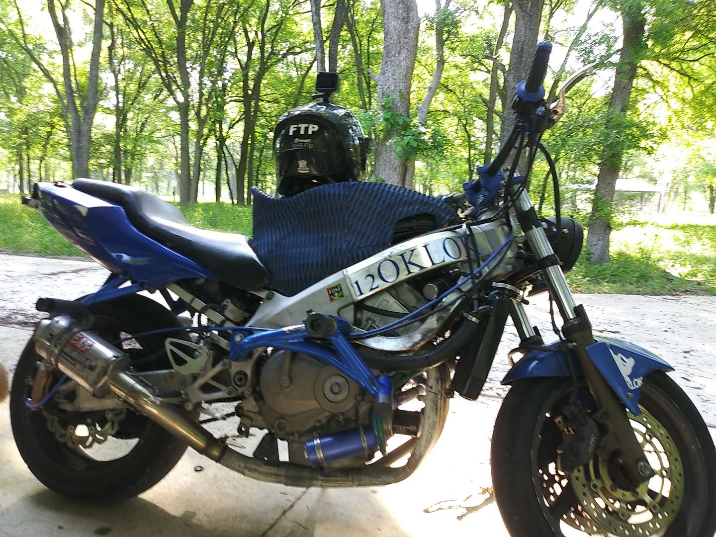 Blue and silver 2000 Honda CBR F4 with stunt modifications and 12OKLOK lettering on the frame, parked under trees