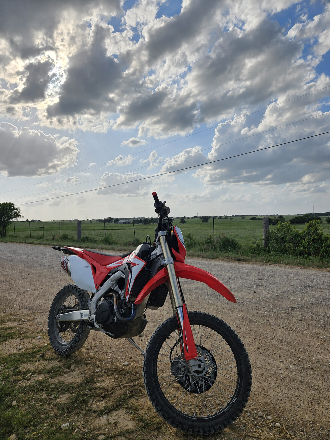 Red and white Honda CRF450 parked beside a gravel road and green fields